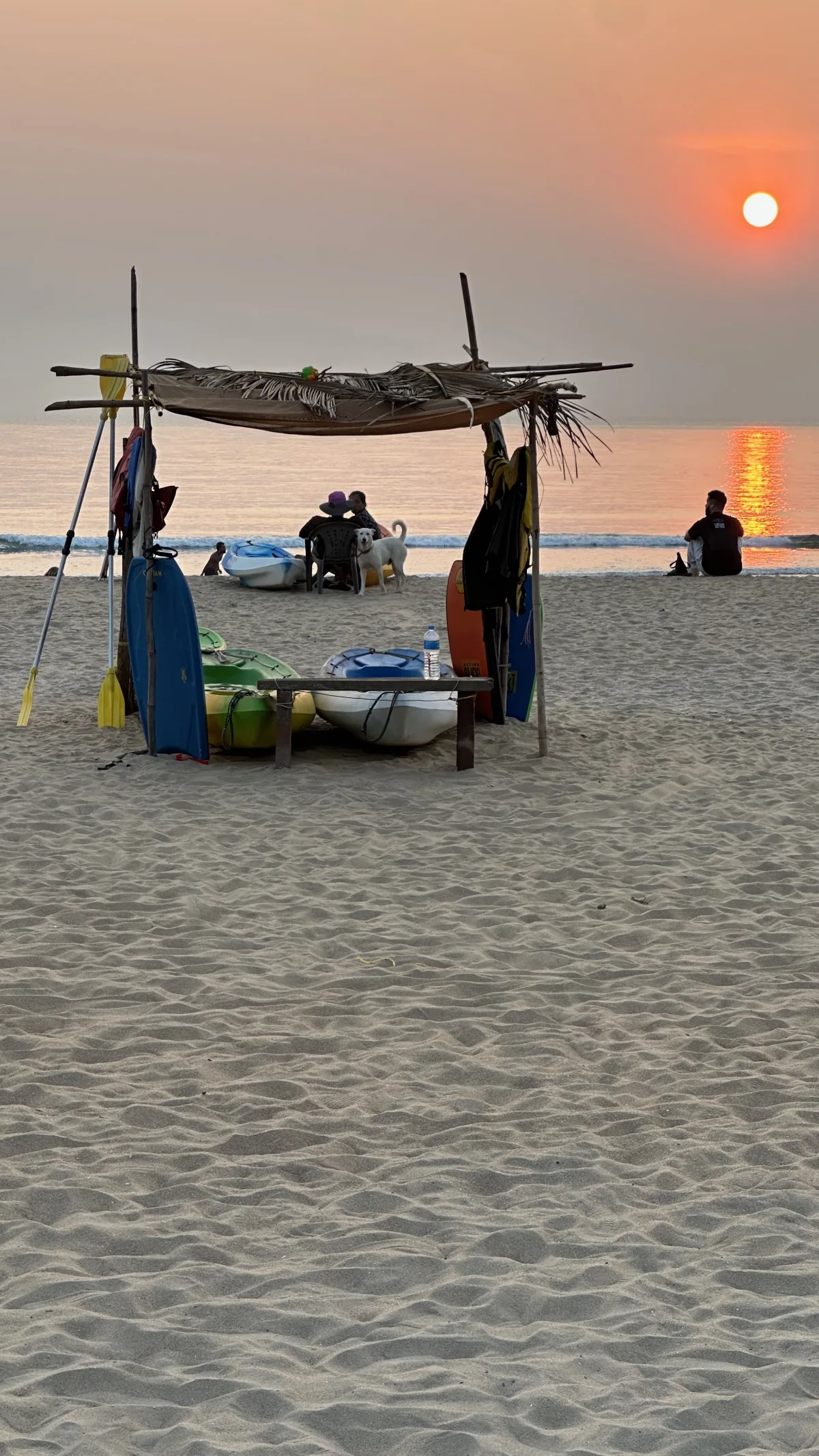 Sunset over the sea at a South Goa beach, with kayaks resting under a palm-thatch shelter