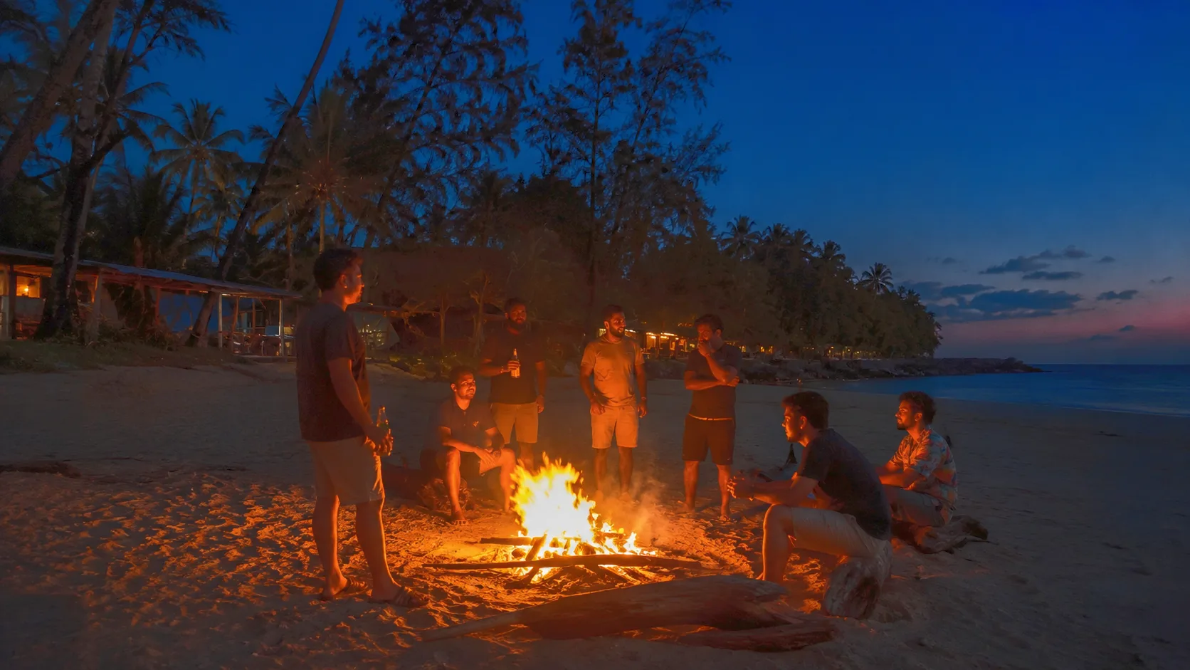 A group of men gathered around a beach bonfire at dusk near The Haven Goa